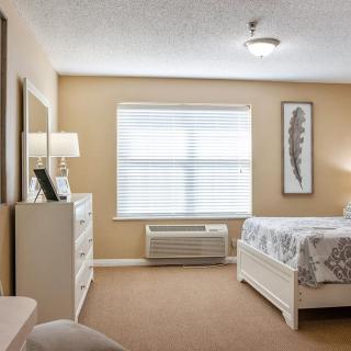 A cozy bedroom with neutral tones, featuring a bed, dresser, and window with blinds.