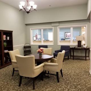 A cozy office meeting room with a round table and chairs, featuring a bookshelf and windows.