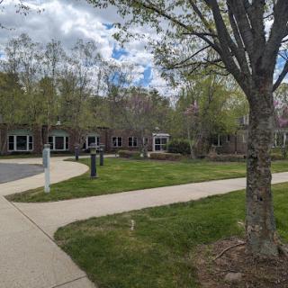 A serene outdoor space featuring a well-maintained pathway, lush greenery, and modern buildings under a partly cloudy sky.
