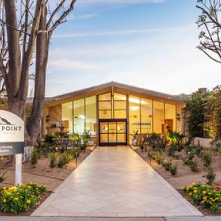 A modern building entrance surrounded by landscaped gardens, illuminated by the warm light of sunset.