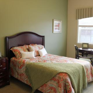 A cozy bedroom featuring a floral patterned bedspread and a desk by the window.