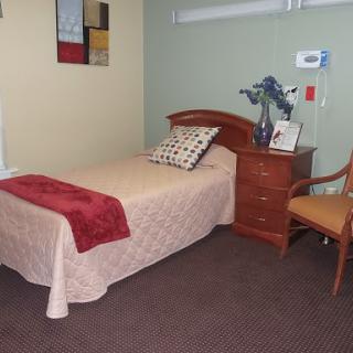 A cozy bedroom featuring a single bed with a light-colored blanket and decorative pillows, alongside a nightstand and a chair.