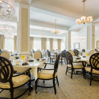 An elegant dining room with neatly arranged tables and chairs, illuminated by chandeliers.