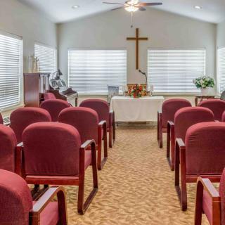 An indoor chapel with rows of red chairs facing an altar and a cross.