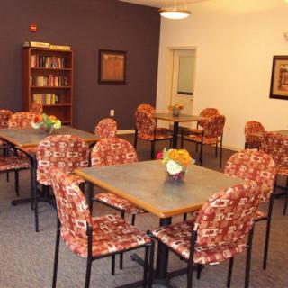 A cozy dining area with multiple tables and chairs, featuring a bookshelf in the corner.