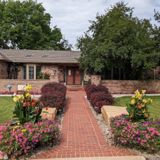 A charming house with a brick pathway leading through a beautifully landscaped garden.