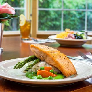 A beautifully plated salmon dish with asparagus, carrots, and peas served on a dining table.