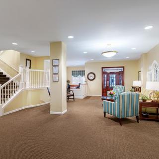 A warmly lit living area with carpeted flooring, featuring a cozy seating arrangement and a staircase.