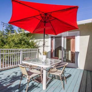A sunny outdoor deck with patio furniture and a vibrant red umbrella.
