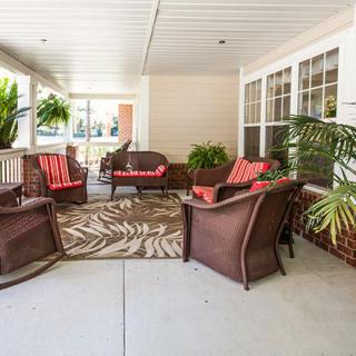 A cozy outdoor patio with rattan furniture, colorful cushions, and lush green plants.