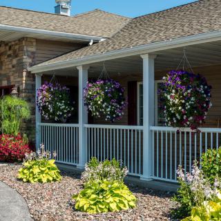 A cozy house with a porch adorned with hanging flower baskets and well-maintained garden landscaping.