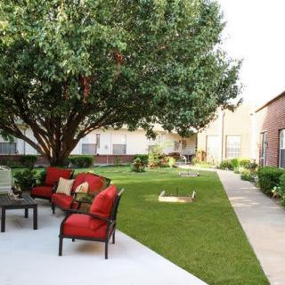 A peaceful backyard with a large tree, patio furniture, and a grassy lawn.