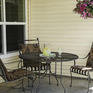 A cozy patio setting with a metal table, three chairs, and a pitcher of lemonade, complemented by a hanging plant.