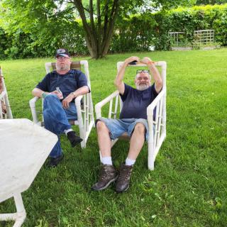 Two people relaxing in chairs on a grassy lawn.