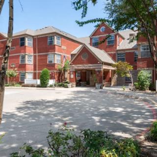 A sunny view of a brick residential building with a welcoming entrance surrounded by trees.
