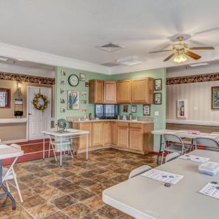 A cozy kitchen area with tables and chairs, featuring a ceiling fan and decorated walls.