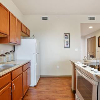 A cozy kitchen with wood cabinets, a refrigerator, and a stove, featuring wood flooring.