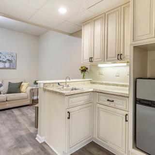 A modern kitchen with cream cabinets and a compact living area in the background.