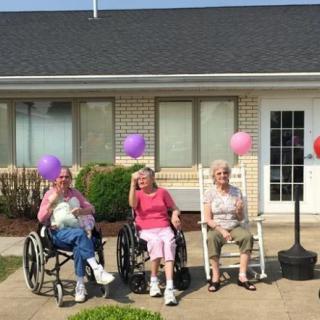 Three elderly people enjoying a sunny day outside, with colorful balloons tied to their chairs.