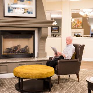 A cozy living room with a fireplace and a person reading in an armchair.