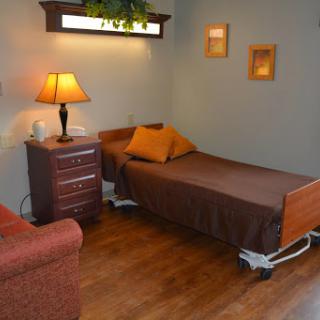 A cozy hospital-style bedroom featuring a single bed, nightstand with a lamp, and a comfortable sofa.