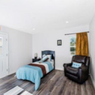A cozy, minimalist bedroom features a single bed with blue bedding and a leather armchair.