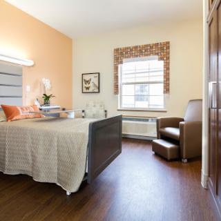 A well-lit hospital room designed for patient comfort, featuring a bed, chair, and window.