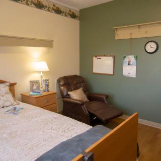 A cozy bedroom with a bed, recliner, and warm lighting.