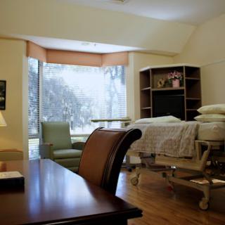 A spacious hospital room featuring a bed, seating area, and natural light streaming through the window.