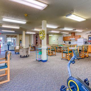 A spacious room with exercise equipment, tables, and chairs under fluorescent lighting.