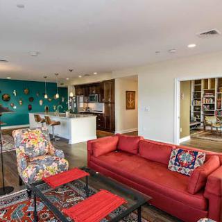 A vibrant and modern living room featuring a red sofa, colorful chairs, and an open kitchen space.