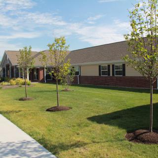 A sunny day at a building with a well-maintained lawn and young trees along a sidewalk.