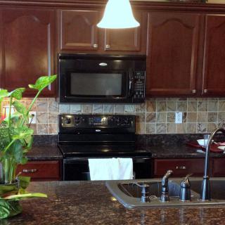 A modern kitchen interior featuring dark wooden cabinets, a black microwave and oven, a granite countertop with a sink, and a decorative plant.