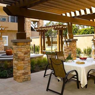 A cozy backyard patio with a pergola and stone pillars, featuring an outdoor dining area set for a meal.