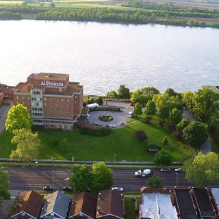 Aerial view of a riverfront building surrounded by lush greenery and residential houses.