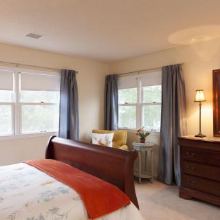 A cozy bedroom with a wooden bed, soft lighting, and large windows adorned with blue curtains.