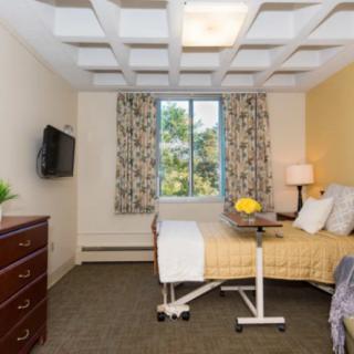 A hospital room with a bed, TV, and a window with patterned curtains.