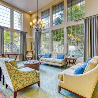 A spacious living room with elegant decor, featuring large windows, a chandelier, and comfortable seating arrangements.