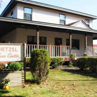 A two-story building with a porch and a sign in the garden.