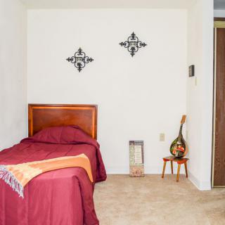 A minimalist bedroom with a single bed featuring red bedding, decorative wall art, and a small side table.