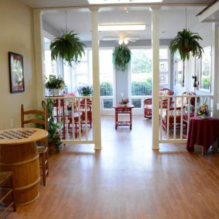 A bright and inviting dining area with wooden floors, featuring tables, chairs, and hanging plants.