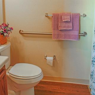 A cozy bathroom with a toilet, pink towels, grab bars, and floral decorations.