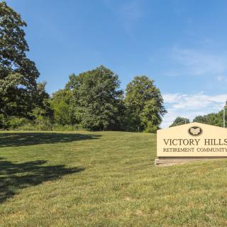 A sign for Victory Hill memorial gardens set in a grassy, tree-lined outdoor area.