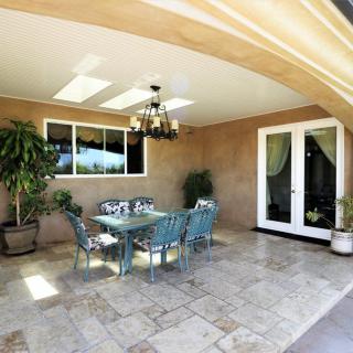 A spacious outdoor patio featuring a dining area with a chandelier, surrounded by potted plants and natural light.