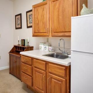 A small kitchen area with wooden cabinets, a white countertop, and a refrigerator.