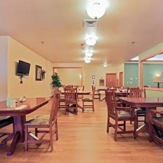 An empty restaurant dining area with wooden tables and chairs, softly lit by ceiling lights.