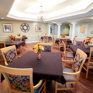 A well-decorated dining room with multiple tables and chairs, featuring floral arrangements and a wooden floor.