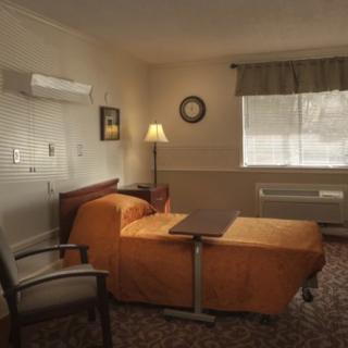 A quiet and simple hospital room with a single bed, chair, lamp, and window with curtains.