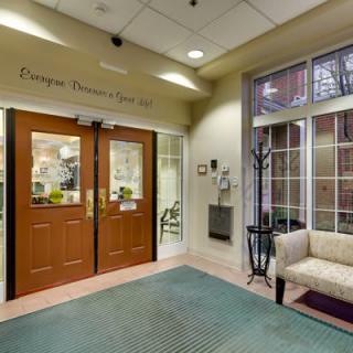The image shows the entrance to a hospital lobby with double wooden doors and a waiting area.