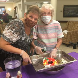 Two women wearing masks and gloves, engaged in a cooking activity indoors.